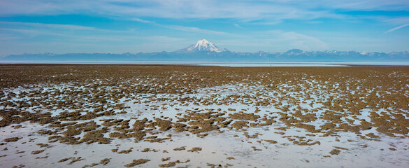 Panorama image of a mountain chain with the glacier capped volcano Mount Redoubt with a muddy tidal...