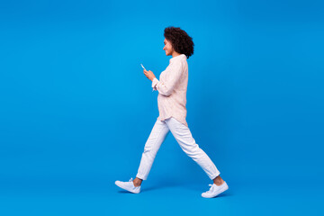 Full length photo of positive sweet lady wear pink shirt walking chatting modern gadget isolated blue color background