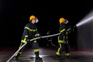 Fototapeta premium Firefighters using a water hose to eliminate a fire hazard. Team of female and male firemen in dangerous rescue mission. 