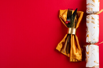 Image of place setting with cutlery, christmas cracker and copy space on red background