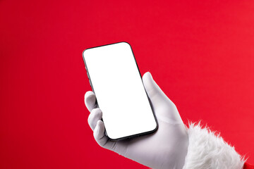 Image of hand of santa claus holding smartphone with blank screen and copy space on red background