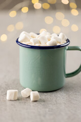 Fototapeta na wymiar Image of green mug with christmas hot chocolate and marshmallows with fairy lights in background
