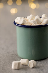 Image of green mug with christmas hot chocolate and marshmallows with fairy lights in background