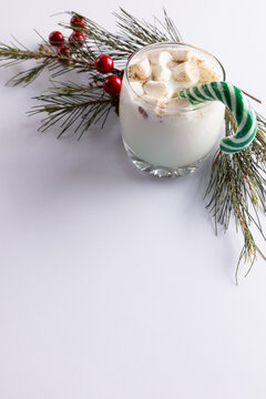 Image of glass of milk with marshmallows, candy cane, christmas decoration and copy space on white