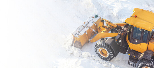 Fototapeta Big orange tractor cleans up snow from the road and loads it into the truck. Cleaning and cleaning of roads in the city from snow in winter. Snow removal after snowfall and blizzards.  obraz