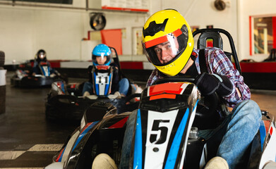 sportive cheerful man and his friends competing on racing cars at kart circuit