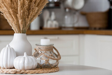 Still-life. Dried pampas grass in a vase, white ceramic pumpkins and a candlestick with a candle on...