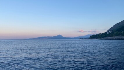 Landscape of the south of Italy from a boat at sunset with high hills, sea till the line of the horizon with past colour in a sunny day