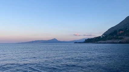Landscape of the south of Italy from a boat at sunset with high hills, sea till the line of the horizon with past colour in a sunny day
