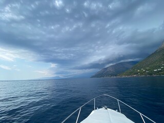 Landscape of the south of Italy from a boat at sunset with high hills, sea till the line of the horizon just before a storm, cloudy sky reflecting on the sea