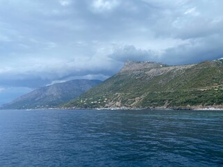 Landscape of the south of Italy from a boat at sunset with high hills, sea till the line of the horizon just before a storm, cloudy sky reflecting on the sea