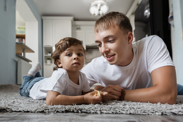 a father and a small child are lying on the floor and playing.