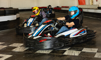 Young positive people in helmets driving go-kart cars in karting club