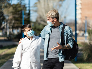Father and son walking to school wearing face mask and a white smock (an Argentinian white coat for...
