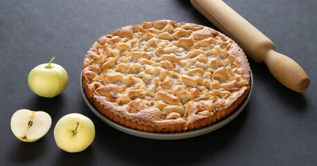 homemade apple pie on a black background in a gray plate with yellow apples and rolling pin