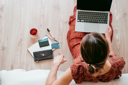 Top View Of Woman In Cute Dress Sitting On The Floor Makes Online Shopping Or Chooses Gifts.