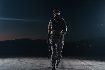 Army soldier in Combat Uniforms with an assault rifle, plate carrier and combat helmet going on a dangerous mission on a rainy night. 