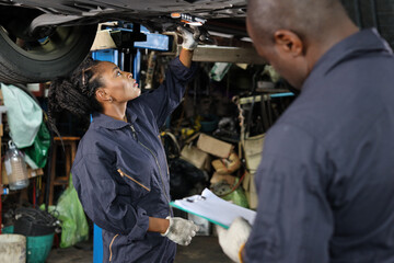 Group of car mechanic in uniform checking maintenance a lifted car service with clipboard at repair garage station. Worker holding wrench and fixing breakdown vehicle. Car repair service concept