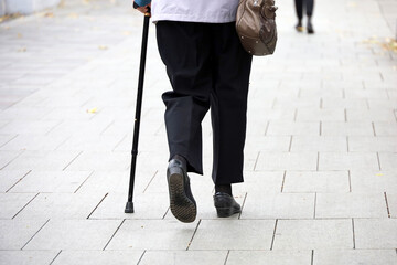Old woman walking with a cane down the city street. Diseases of the spine and legs of elderly people
