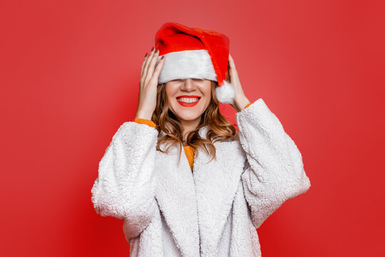woman in festive christmas hat and white faux fur coat fooling around isolated over red background