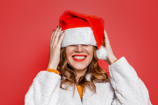 woman in a festive christmas hat and white faux fur coat fooling around isolated over red background