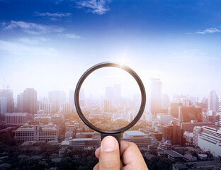 A man's hand holding a magnifying glass of the cityscape highlighting the business vision background