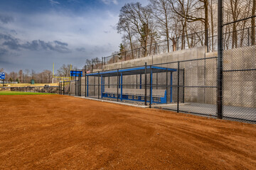 View of typical nondescript high school softball clay infield from infield near home plate looking toward the first base dugout.  No people visible.  Not a ticketed event.		