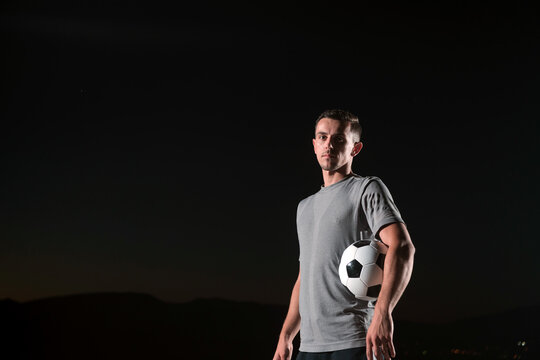 portrait of a young handsome soccer player man on a street playing with a football ball.