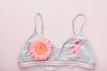 Pink Breast Cancer Awareness Ribbon. Gerbera and pink ribbon tape lying on female white bra on backgrounds. Breast cancer awareness and October Pink day, world cancer day. Top view. Mock up.