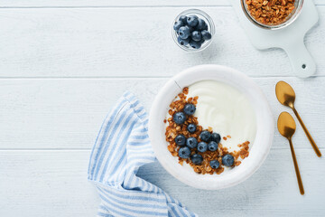 Yogurt. Greek Yogurt with granola and fresh blueberries in white bowl over old white wood background. Morning breakfast concept. Healthy food for breakfast, top view