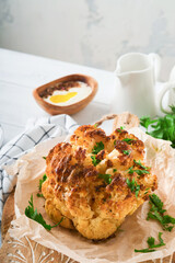 Baked cauliflower. Oven or whole baked cauliflower spices and herbs server on wooden rustic board on old white wooden background table. Delicious cauliflower. Eyal Shani dish. Perfect tasty snack.