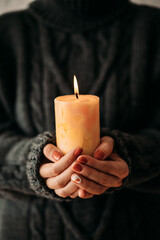 A woman in a cozy sweater holds a burning candle close-up. Cozy autumn or winter, the concept of comfort and coziness.