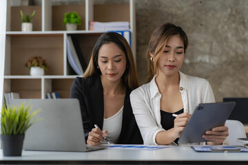 A team of Asian businesswomen discussing something and smiling as they sit at a desk in the office of women working together analyzing finances.