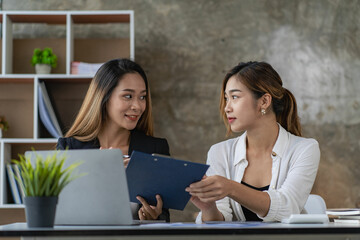 A team of Asian businesswomen discussing something and smiling as they sit at a desk in the office of women working together analyzing finances.