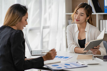 Obraz premium A team of Asian businesswomen discussing something and smiling as they sit at a desk in the office of women working together analyzing finances.