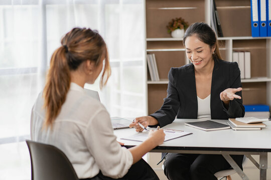Workplace job idea Asian beautiful woman talks to hr manager for office job interview Attractive woman sits at a desk and gives her HR manager a business resume with a handshake at the reception.