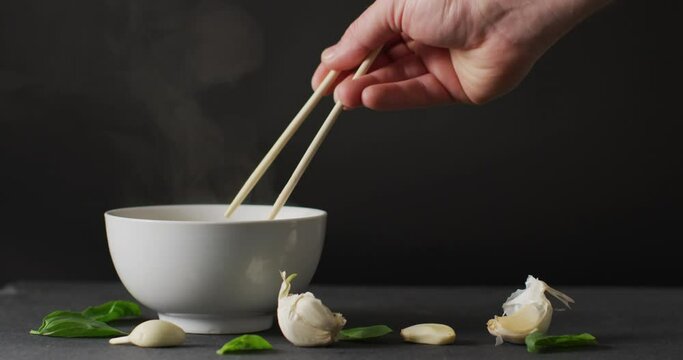 Hand holding chopsticks with noodles in bowl on black background