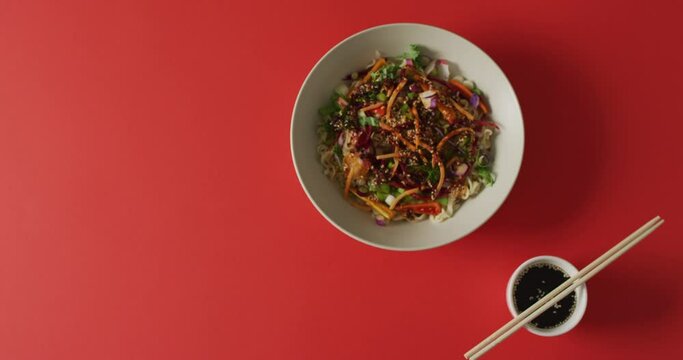 Composition of bowl of stir fry noodels with soy sauce and chopsticks on red background