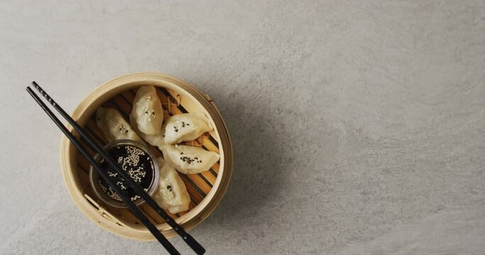 Composition of bamboo steamer with gyoza dumplings and chopsticks with soy sauce on grey background