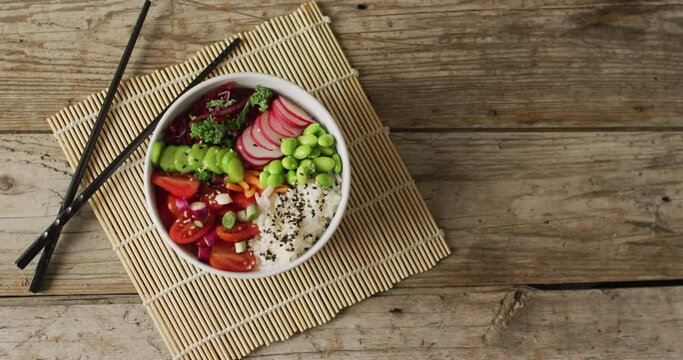 Composition of bowl of rice and vegetables with chopsticks on wooden background