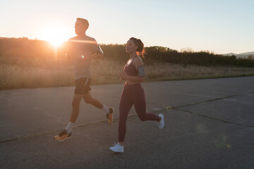 Fototapeta premium healthy young couple jogging in the city streets in the early morning with a beautiful sunrise in the background. 
