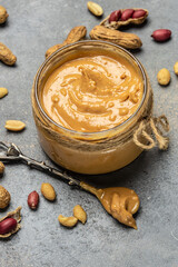 Peanut butter in glass jar and spoon on gray background, American dessert concept. vertical image. top view. place for text