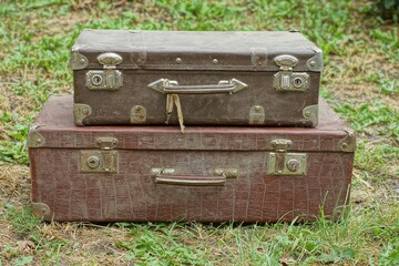 two old handmade retro suitcases of dark and brown color with iron rusty latches lie on the street on the green grass during the day