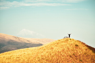 Naklejka na ściany i meble Top view inspirational excited joyful caucasian male cyclist stand on hilltop by red touring bicycle excited enjoy Ararat mountains background. Solo cycling adventure lifetime