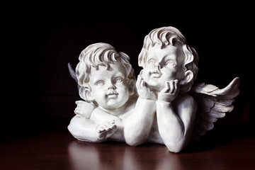 White angels on a dark background. The angels rest their face on their hands and dreamily look into the distance