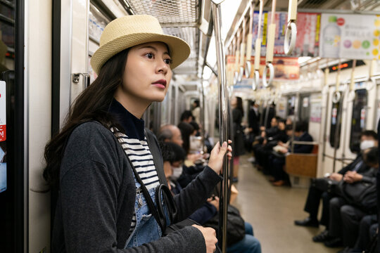beautiful Asian Japanese girl wearing hat traveling by taking subway in nara-shi japan. she holds the pole and looks at space while standing in the train car.