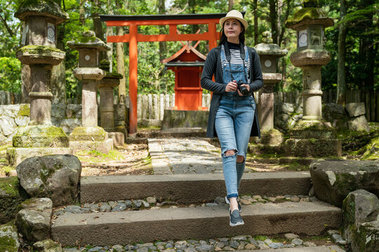 full length of Asian Japanese female tourist using stairs while exploring in the park with red torii gate and stone lamps near Kasuga Grand Shrine in nara japan.