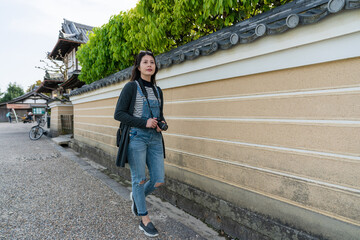 full length of leisure asian Japanese woman photographer walking alone fence wall at the exterior...