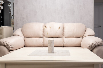 A coffee table, a vase with a lagurus and a sofa in a modern interior.