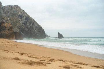 Ocean wild beach stormy weather. Praia da Adraga sandy beach with picturesque landscape background, Sintra Cascais, Portugal